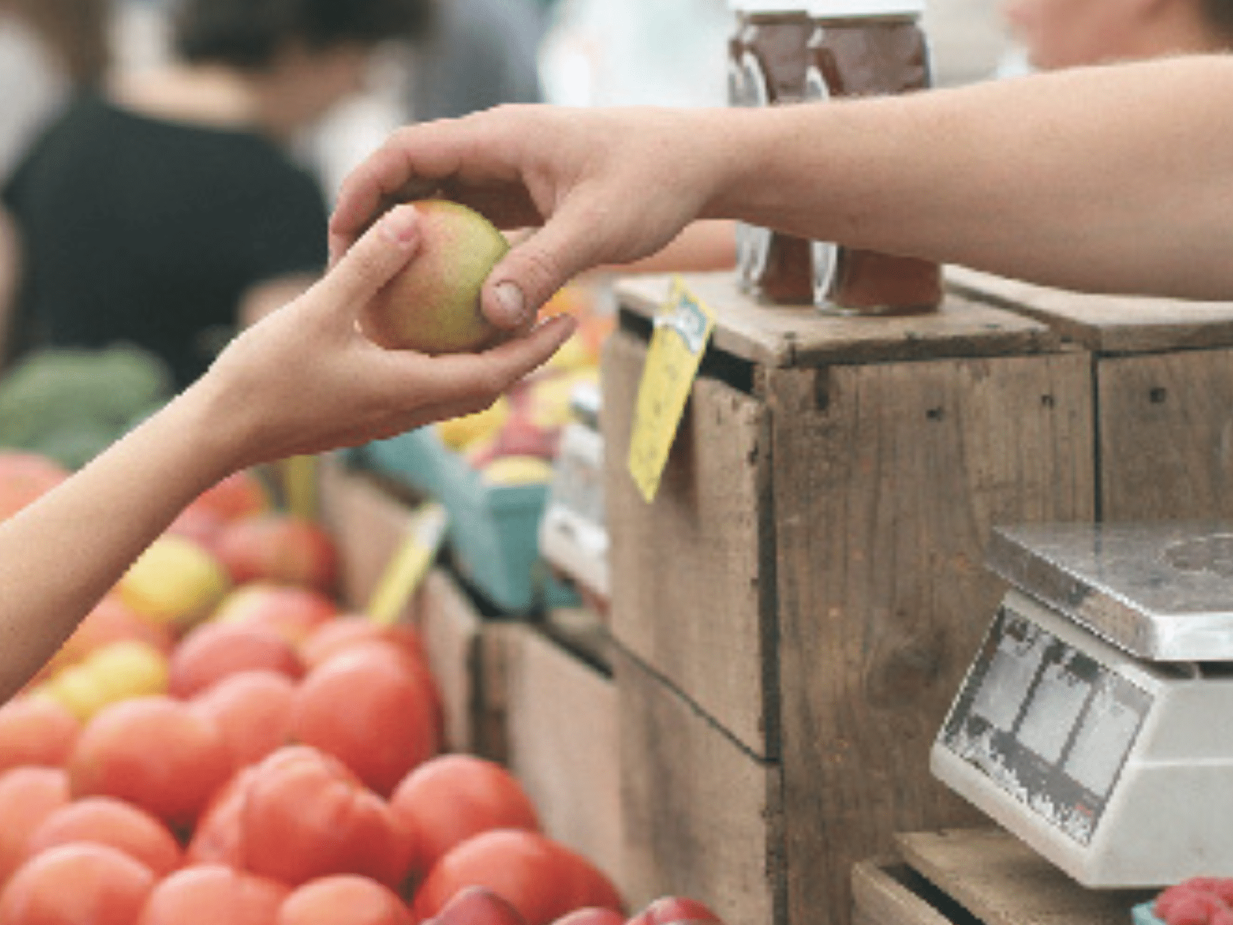 An image showing the hands of two individuals exchanging apples in a market place.