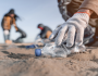 Volunteers cleaning up a beach littered with plastic debris. End plastic pollution. Every action counts.