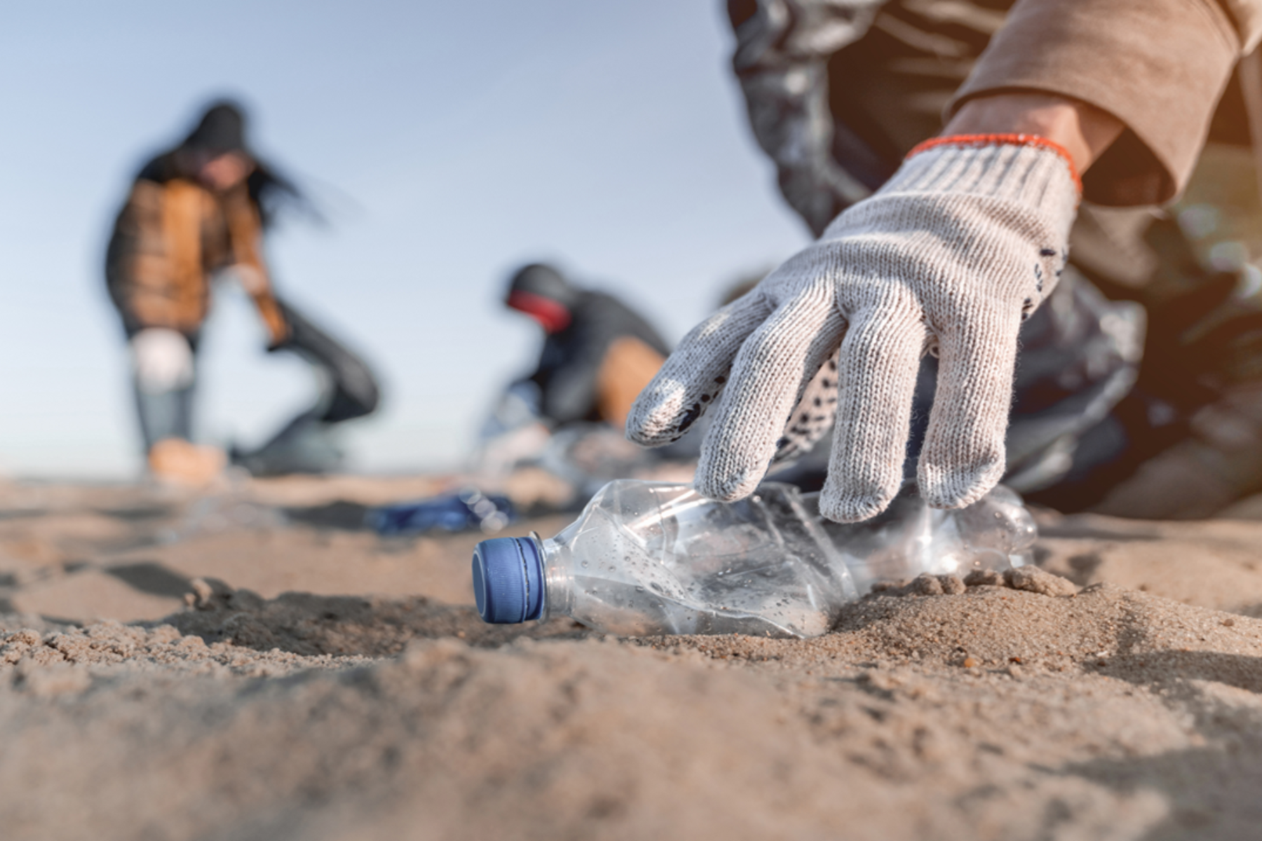 Volunteers cleaning up a beach littered with plastic debris. End plastic pollution. Every action counts.